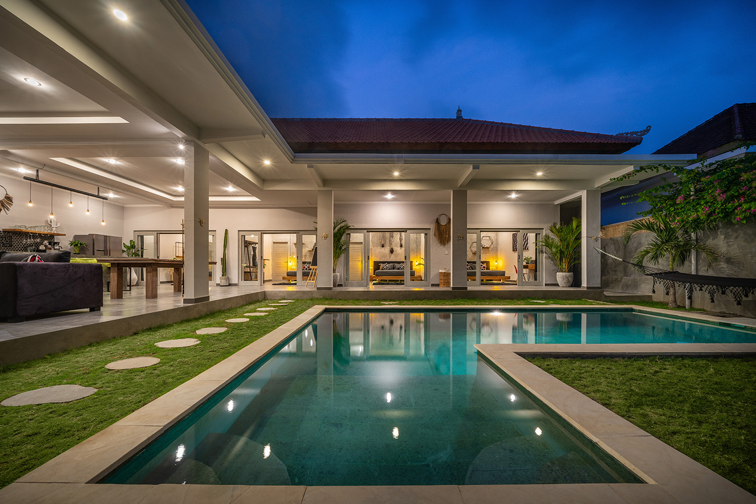Tropical villa view with garden, swimming pool and open living room at sunset